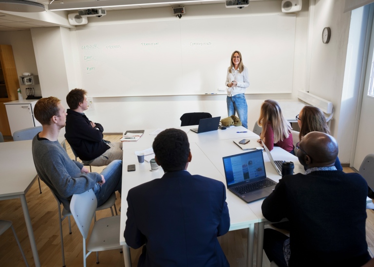 Kvinnlig lärare undervisar studenter i klassrum.