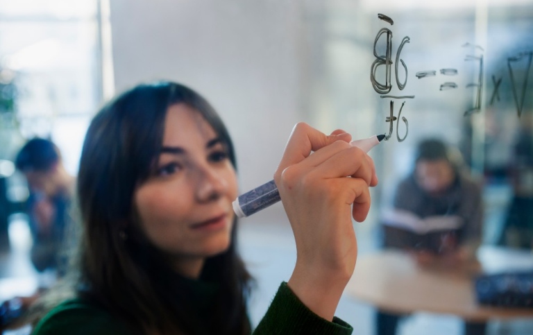 A woman is writing a formula on a glass wall.