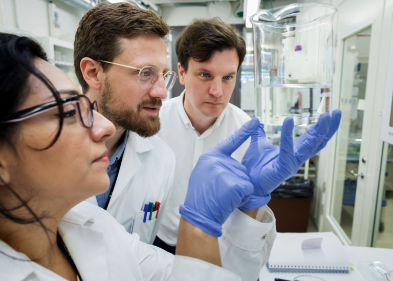 Tre forskare i labbet, tittar på glaskolv