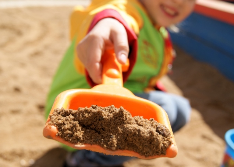 Barn sträcker fram en spade med sand.