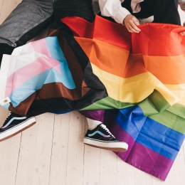 Two people unfolding an LGBTQIA+ flag. Photo from Pexels