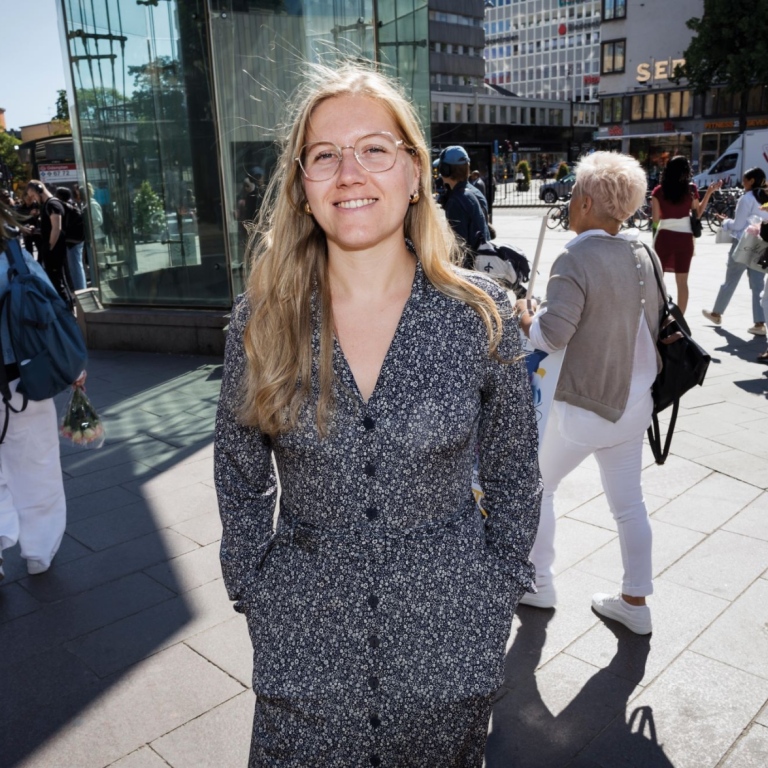 Elin Hellström står på ett torg och människor passerar i bakgrunden.