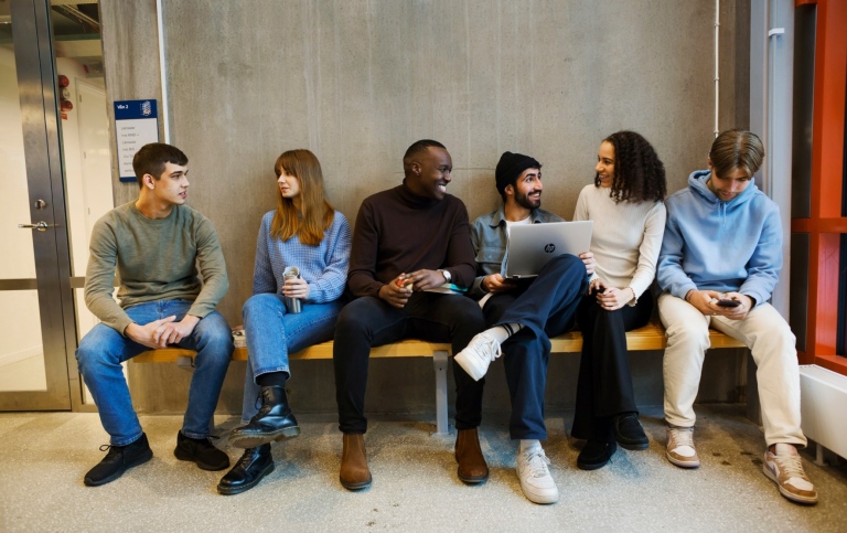 Sex glada studenter sitter på en bänk och pratar.