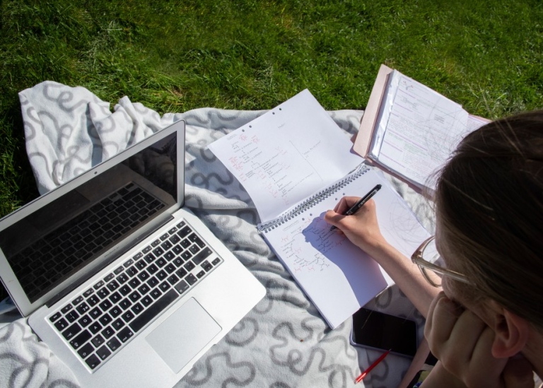 Student sitter i gräset och pluggar.