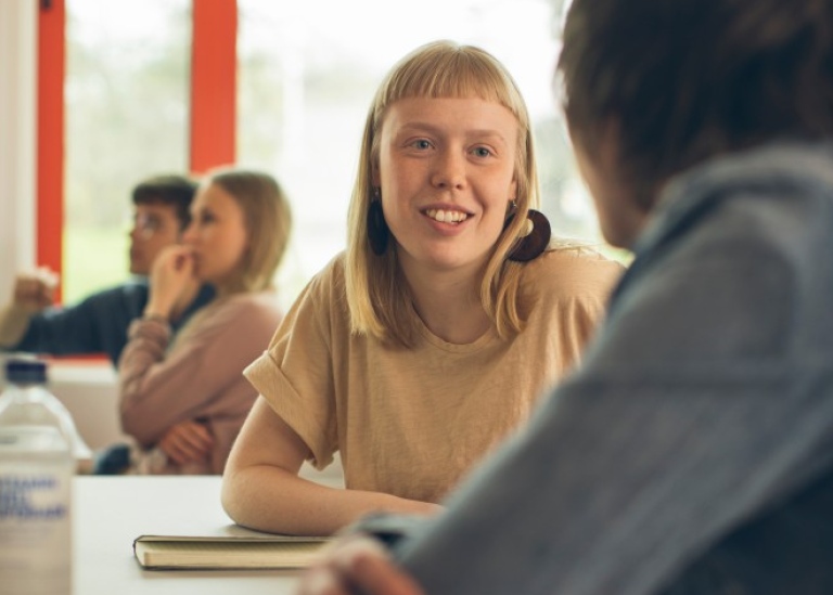 Två studenter sitter och pratar, den ena med ryggen mot kameran. Två studenter o önster i bakgrunden