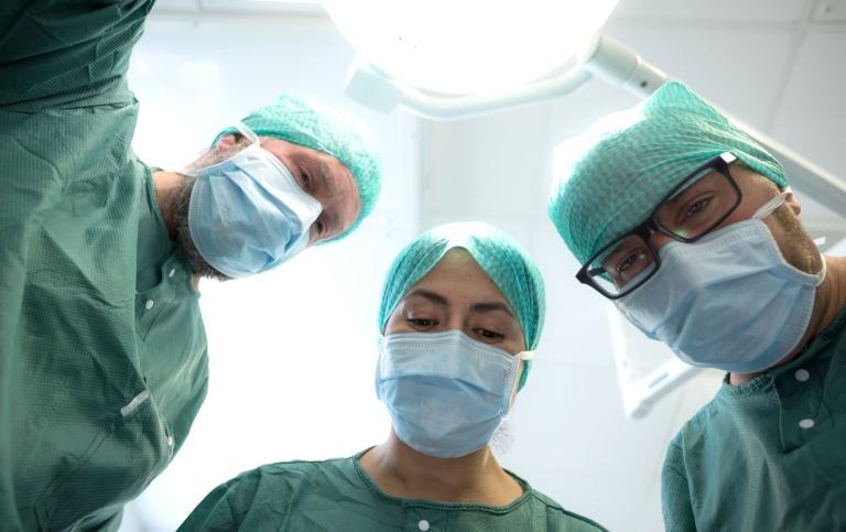 Tre operationsklädda läkare i grönt lutar sig fram mot kameran.