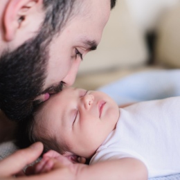 En ung far kysser sin sovande nyfödda son. Far och nyfödd baby i närbild. Far och nyfödd ligger på s