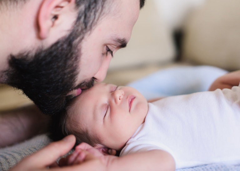 A young father kisses his sleeping newborn son. Father and newborn baby closeup. Father and newborn