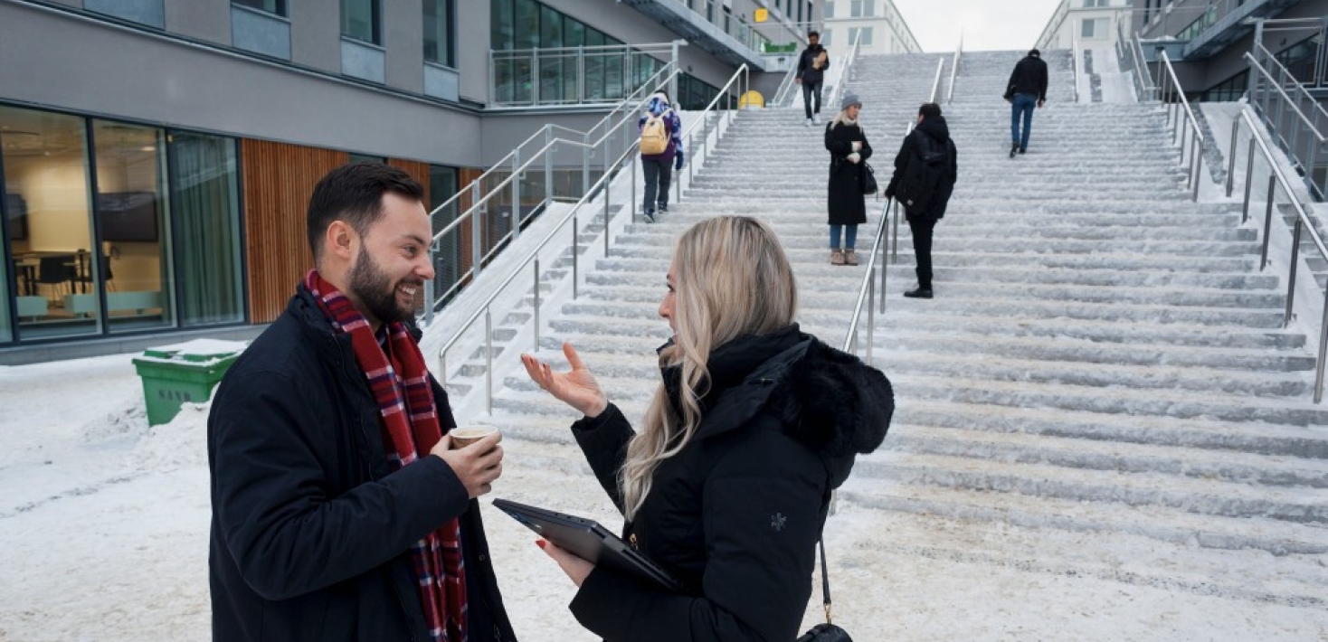 Campus Albano, two people talking to each other by a staircase.