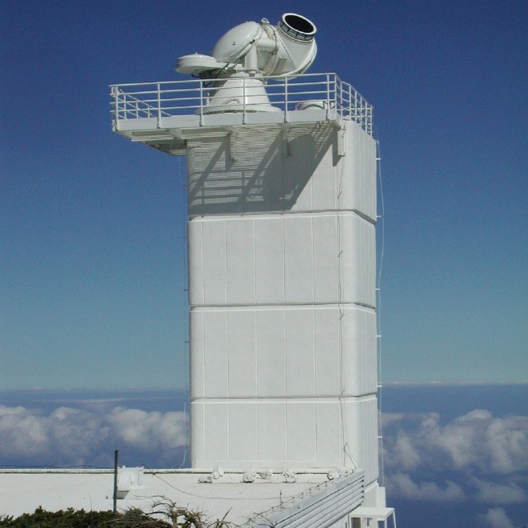 Ett vitt torn med moln i bakgrunden. På tornets topp syns en teleskopöppning