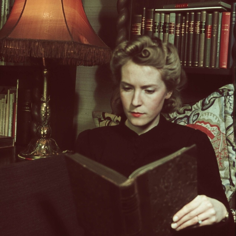 En kvinna sitter och läser en bok vid en lampa.