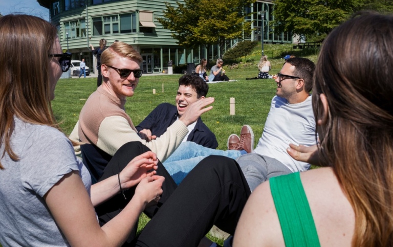 Glada studenter sitter utomhus på gräsmatta.