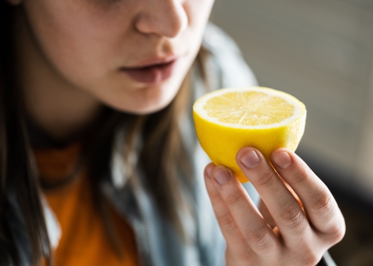 Close up picture of a woman smelling a lemon half.