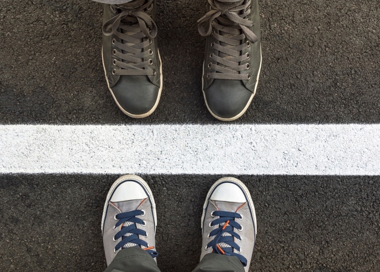 Bild på två par fötter stående mittemot varandra med en målad bred linje på asfalten mellan dem.
