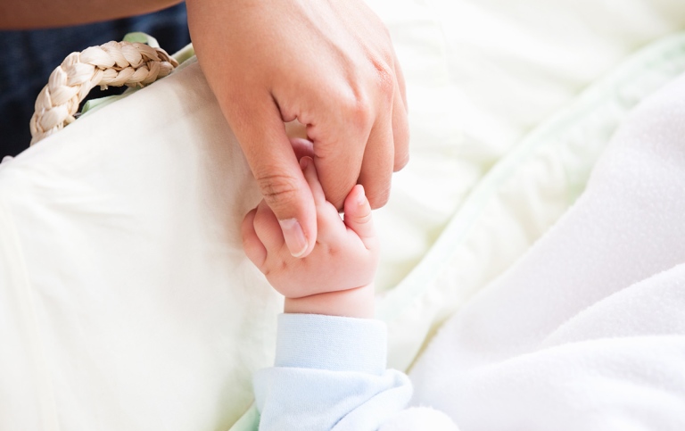 Närbild av en ung mamma som håller sitt barn i handen.