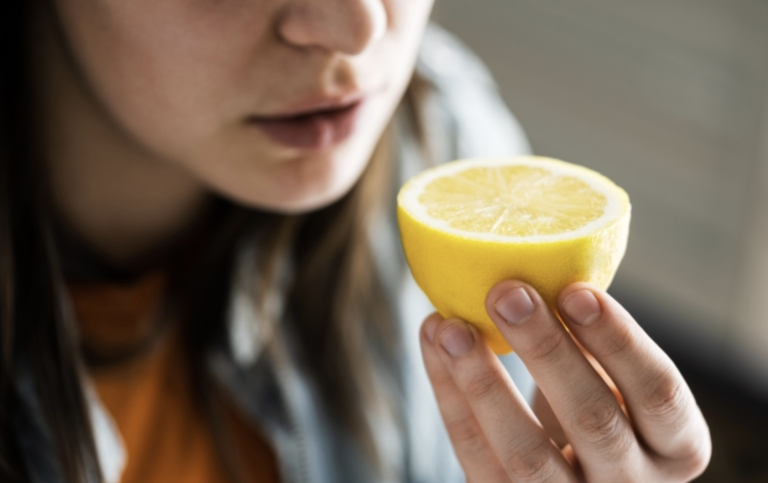 Kvinna håller en citronhalva framför näsan