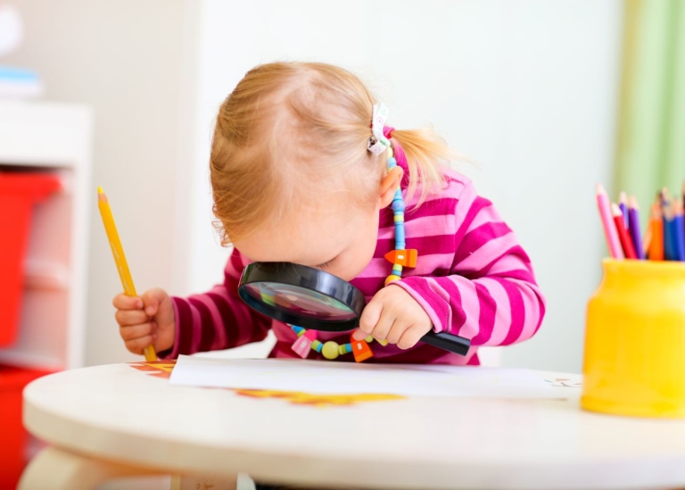 Litet barn närstuderar en bild med förstoringsglas.