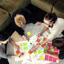 Four people working together over a table filled with colorful post-it notes.