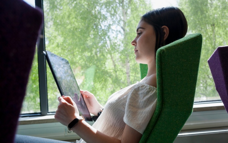 Kvinnlig student som sitter i grön fåtölj och tittar på en dator.