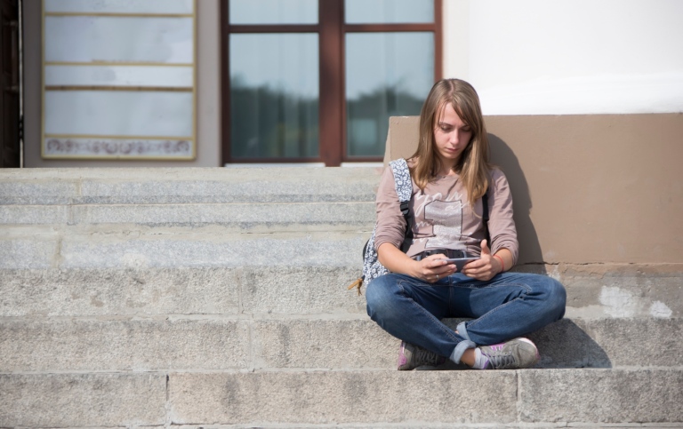 A lonely girl with a phone sits on the steps