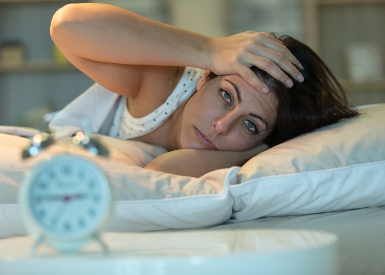 Woman lying awake in bed, looking tired.