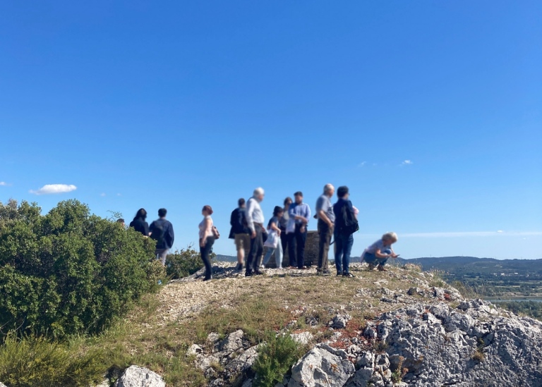 En grupp människor står på ett berg med utsikt över en dal. Blå himmer och sol.