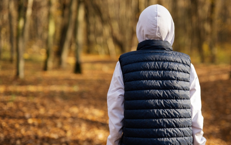 Back portrait of teen boy in hoodie and sleeveless vest at fall forest.