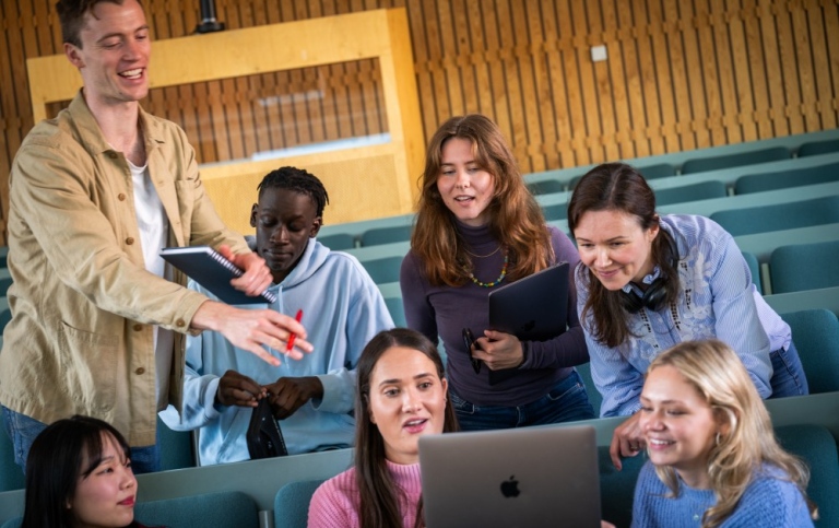 Studenter som diskuterar innehåll på laptop i föreläsningssal. 