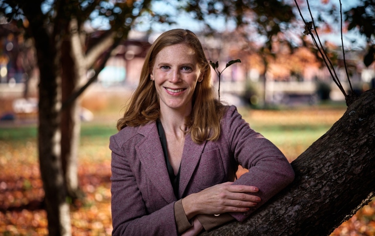 Foto utomhus på Lia Bahizi som lutar armen på ett träd. Höst.