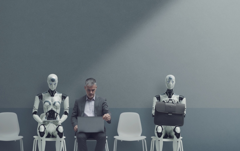 A middle-aged man in a suit sits working on a laptop, flanked by two humanoid robots.