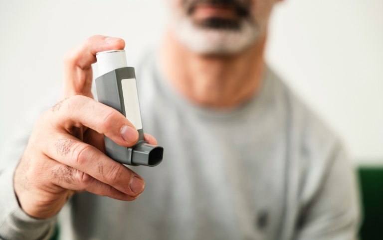 A man holding his asthma inhaler.