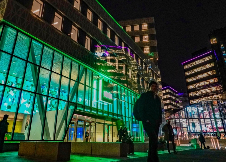 A person standing in front of an enlightened office building.