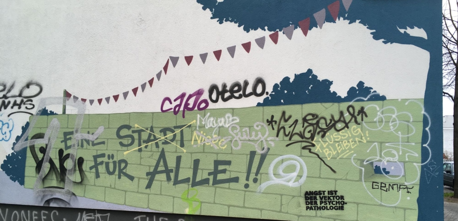 A city wall with graffiti, the text "a city for all" as one of them.