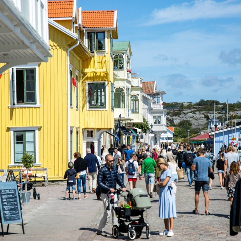 A sunny summer day in a Swedish coastal town, with colorful wooden houses and people strolling.