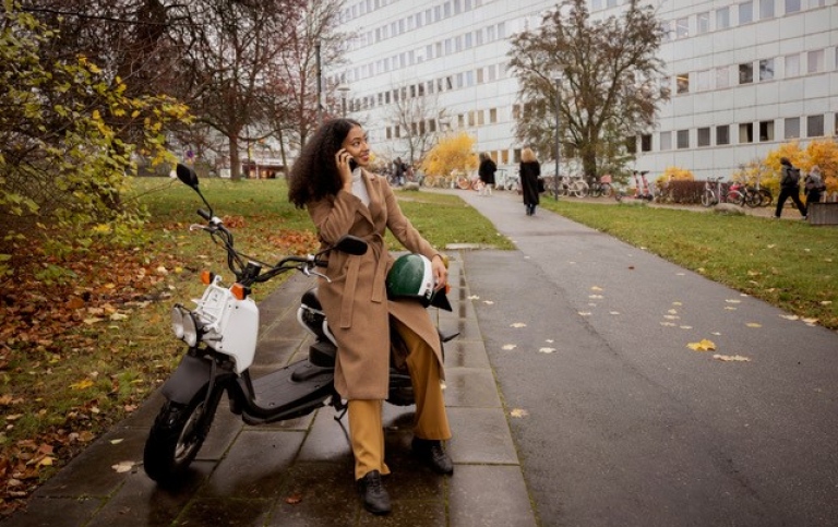 Woman leaning against a scooter with a mobile phone in her hand.