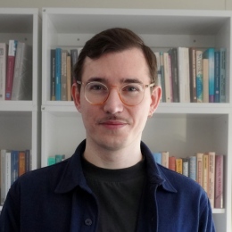 30-something male with glasses in front of bookshelves