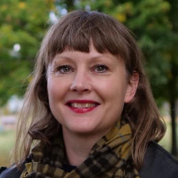 En bild av en leende Sofie Wennström med en parkmiljö i bakgrunden.