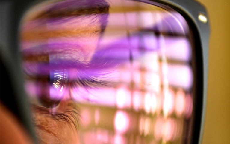 Close-up of a person's eye, they are wearing glasses reflecting the world. 