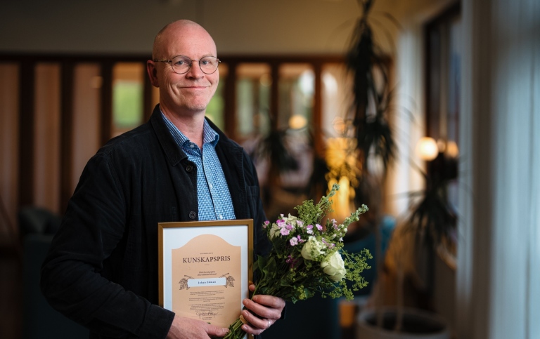 Johan Edman ler mot kameran och håller i ett diplom och blomsterbukett.
