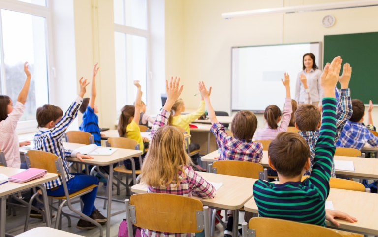 Grupp av elever i klassrum som räcker upp händerna.