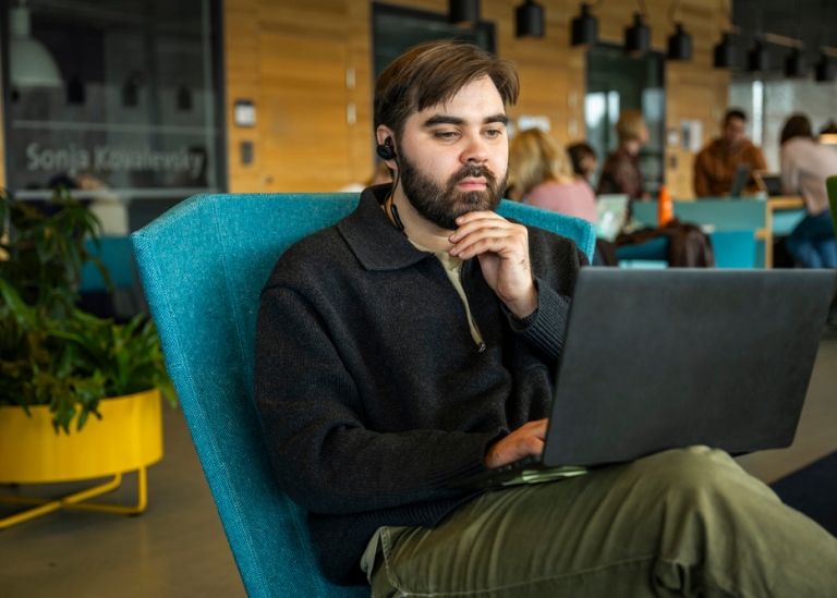 Manlig student som sitter i Studenthuset och tittar på sin laptop.