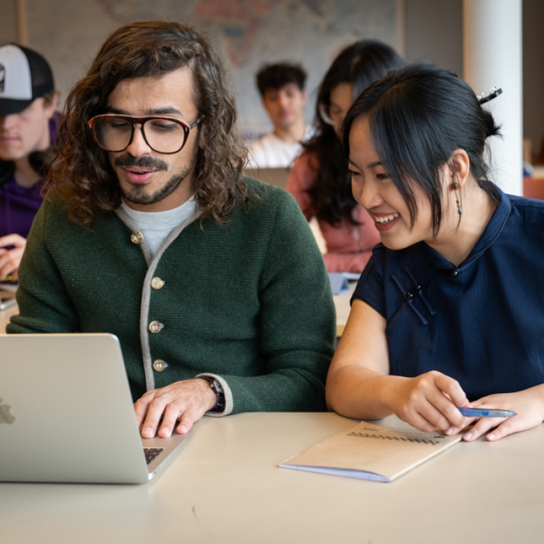 Två studenter framför en dator i en föreläsningssal.