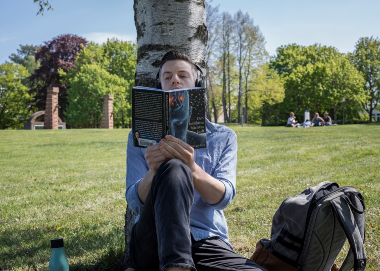 Man sitter och läser en bok under ett träd.