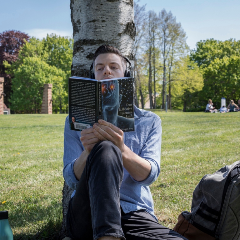 Man sitter och läser en bok under ett träd.