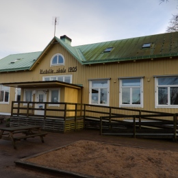 Gul trähusbyggnad med grönt plåttak. Text på huset: Kvibille skola 1905.