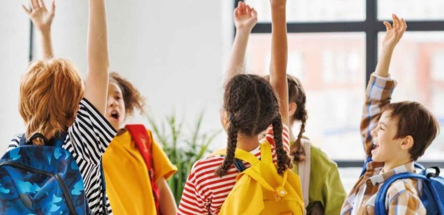 A group of children in colorful clothes raise their arms and shout.