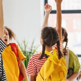 A group of children in colorful clothes raise their arms and shout.