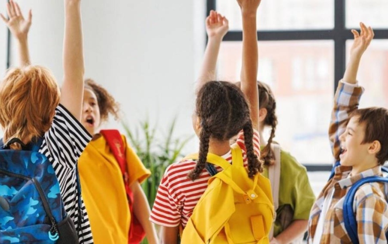 A group of children in colorful clothes raise their arms and shout.