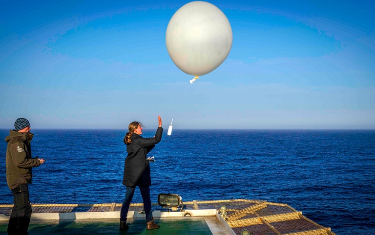 Student releasing big white balloon in the air. Blue water and blue sky