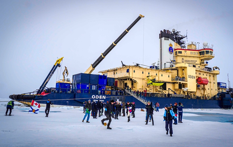 People playing on the ice, with icebreaker Oden in the vackground.
